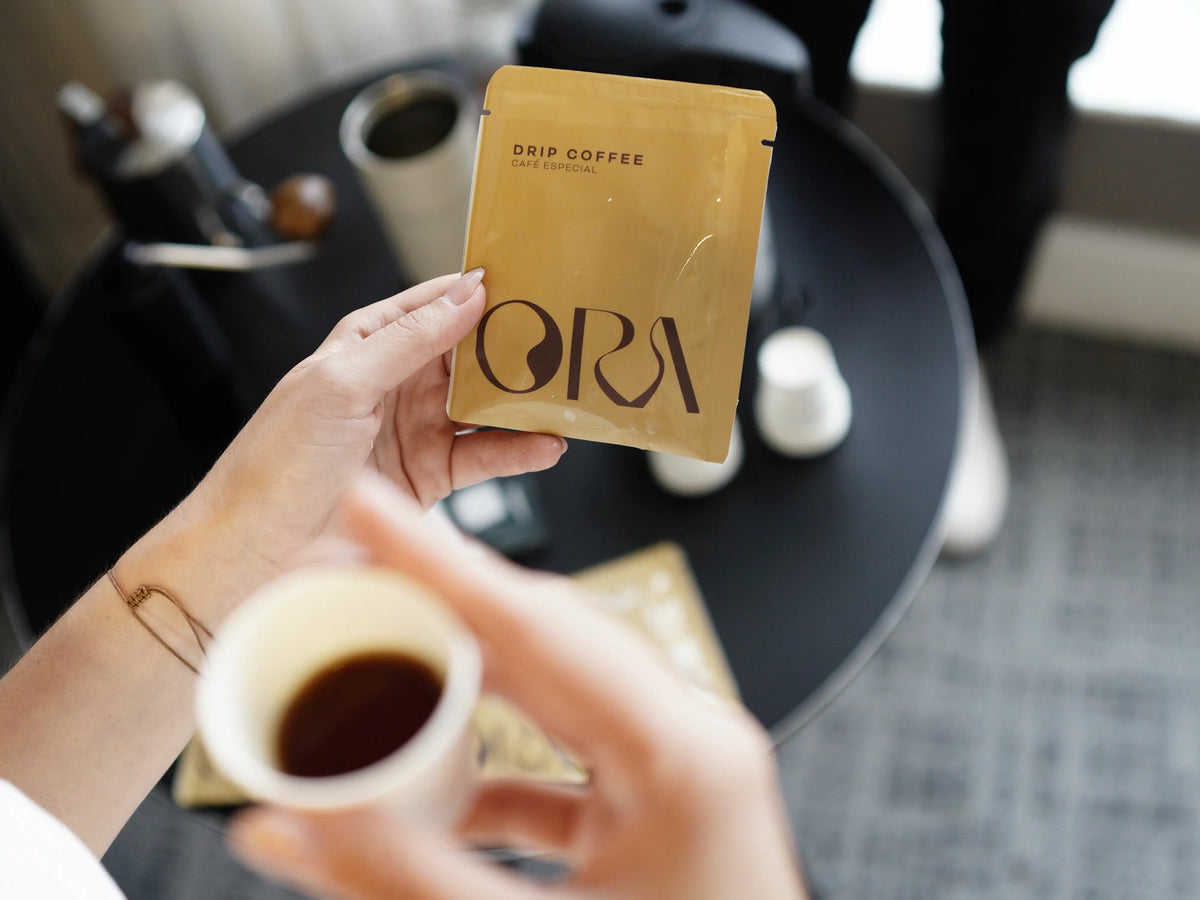 Sachê de drip coffee com a marca ORA, café especial personalizado pela ZinGrão, e xícara de café coado à frente