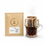 Sachê de Drip Coffee Intenso Chocolate ZinGrão ao lado de xícara de vidro com o filtro individual em extração, café especial de Matas de Minas